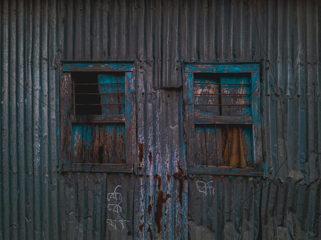 Corrugated metal building with two rustic windows, showcasing decay and weathering.