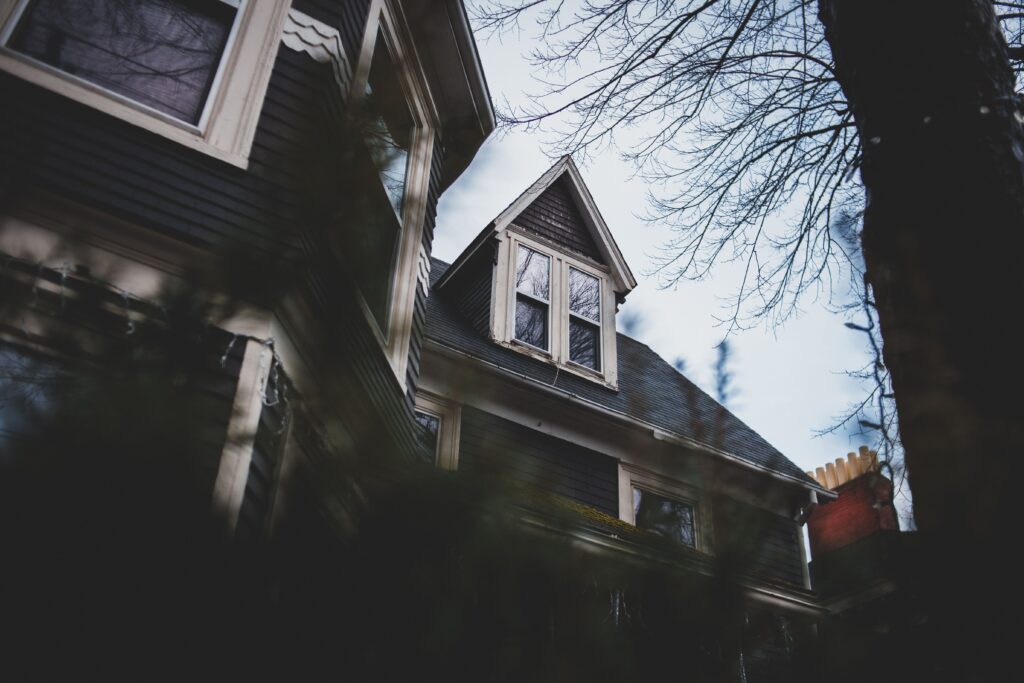 From below of house with white wooden window frames and attic surrounded with trees and green bushes